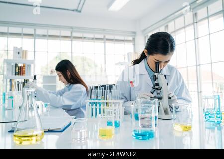 Gros plan de l'équipe asiatique de recherche scientifique féminine en protection équipement utilisant un microscope dans le laboratoire pour développer un vaccin antivirus Banque D'Images