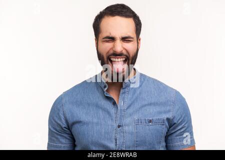 Naughty ininfantile homme avec la barbe fermer les yeux et montrant la langue, s'amuser, se moquer autour, les manières puériles. Prise de vue en studio isolée sur b blanc Banque D'Images