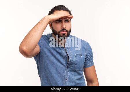 Homme barbu attentif regardant loin à distance avec la main sur la tête, recherchant avec attention pour un avenir brillant. Prise de vue en studio isolée sur blanc Banque D'Images