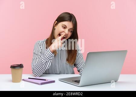 Femme paresseuse de bureau ayant le plaisir de prendre le nez et regardant dans l'écran d'ordinateur portable avec l'expression imprudente, parlant sur appel vidéo sur le lieu de travail. Intérieur s Banque D'Images