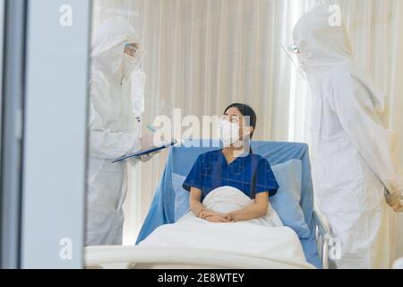 Groupe de spécialistes de la quarantaine Covid-19 en uniforme d'epi travaillant avec un patient infecté par le virus corona dans la salle de contrôle de l'hôpital. Concept de traitement et de prévention du coronavirus Banque D'Images