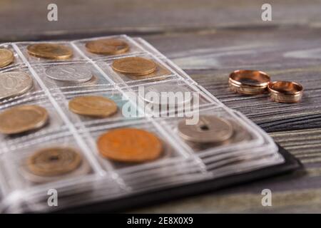 Livre avec collection de pièces de monnaie et anneaux de mariage. Banque D'Images