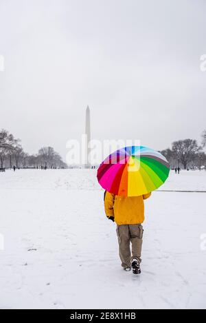 Un homme porte un parapluie coloré pendant une journée enneigée sur le National Mall à Washington, D.C. le Washignton Monument peut être vu au loin. Banque D'Images