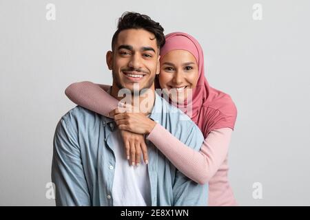 Portrait d'un couple musulman embrassant sur fond gris et souriant À la caméra Banque D'Images