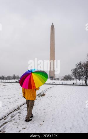 Un homme porte un parapluie coloré pendant une journée enneigée sur le National Mall à Washington, D.C. le Washignton Monument peut être vu au loin. Banque D'Images