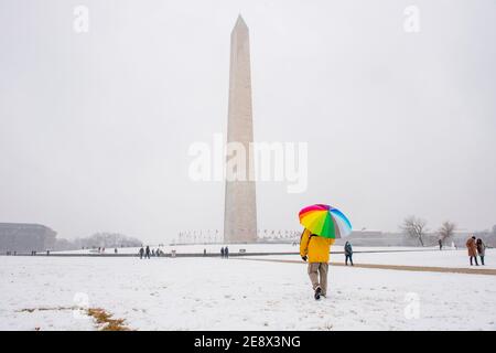 Un homme porte un parapluie coloré pendant une journée enneigée sur le National Mall à Washington, D.C. le Washignton Monument peut être vu au loin. Banque D'Images