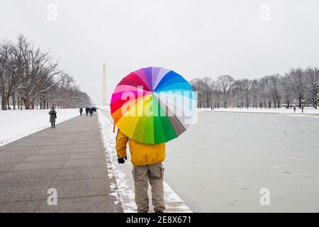 Un homme porte un parapluie coloré pendant une journée enneigée sur le National Mall à Washington, D.C. le Washignton Monument peut être vu au loin Banque D'Images