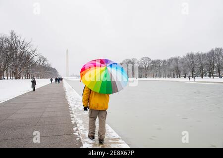 Un homme porte un parapluie coloré pendant une journée enneigée sur le National Mall à Washington, D.C. le Washignton Monument peut être vu au loin Banque D'Images