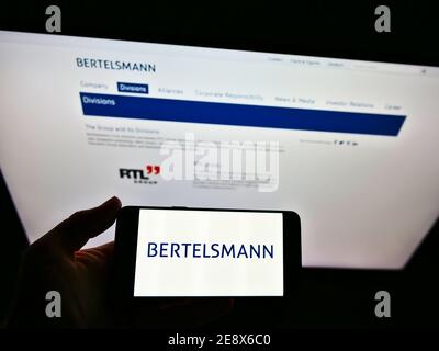 Personne tenant un smartphone avec le logo du conglomérat allemand des médias de masse Bertelsmann exposé devant le site Web. Mise au point sur l'écran du téléphone mobile. Banque D'Images