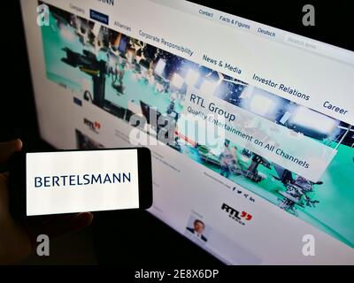 Vue en grand angle de la personne qui tient un smartphone avec le logo du conglomérat allemand des médias de masse Bertelsmann exposé. Mise au point sur l'écran du téléphone mobile. Banque D'Images