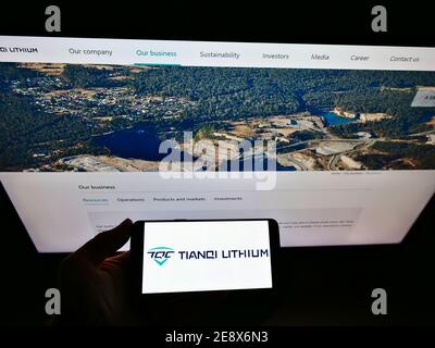 Vue à grand angle de la personne tenant le téléphone mobile avec le logo de la société chinoise de fabrication Tianqi Lithium Corp sur l'exposition. Mise au point sur l'écran du téléphone portable. Banque D'Images