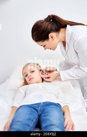 perçage des oreilles à l'enfant caucasien fille dans le salon médical par un médecin en robe blanche en utilisant un dispositif spécial. beauté et médecine concept Banque D'Images