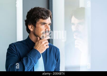 Homme d'affaires regardant par la fenêtre. Portrait réussi de sexe masculin au bureau avec le bon foyer, attitude sérieuse et sereine. Banque D'Images
