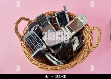 panier en osier, avec téléphones mobiles cassés, technologie de recyclage, début des années 2000 sur fond rose et espace de copie,. Banque D'Images