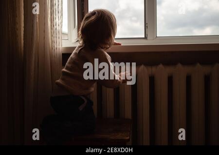 L'enfant monte à la fenêtre, la fille sur le seuil de la fenêtre repose sur le filet, le danger de tomber. L'enfant est seul à la maison, peut tomber du Banque D'Images