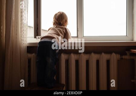 L'enfant monte à la fenêtre, la fille sur le seuil de la fenêtre repose sur le filet, le danger de tomber. L'enfant est seul à la maison, peut tomber du Banque D'Images