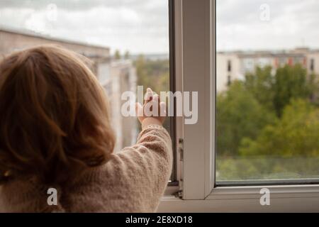 L'enfant monte à la fenêtre, la fille sur le seuil de la fenêtre repose sur le filet, le danger de tomber. L'enfant est seul à la maison, peut tomber du Banque D'Images