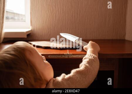 L'enfant tire un couteau de la table, danger. L'enfant peut couper, les dangers à la maison des enfants. Une petite fille d'un an avec un couteau. Banque D'Images