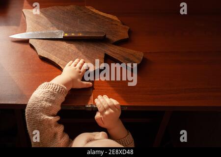 L'enfant tire un couteau de la table, danger. L'enfant peut couper, les dangers à la maison des enfants. Une petite fille d'un an avec un couteau. Banque D'Images