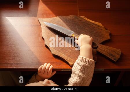 L'enfant tire un couteau de la table, danger. L'enfant peut couper, les dangers à la maison des enfants. Une petite fille d'un an avec un couteau. Banque D'Images