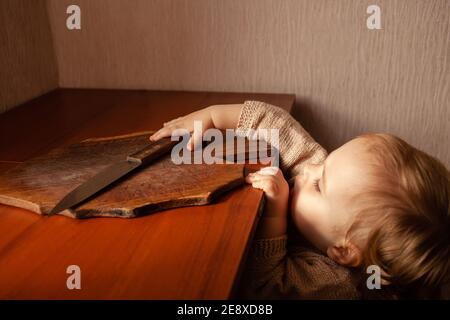 L'enfant tire un couteau de la table, danger. L'enfant peut couper, les dangers à la maison des enfants. Une petite fille d'un an avec un couteau. Banque D'Images