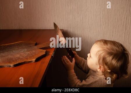 L'enfant tire un couteau de la table, danger. L'enfant peut couper, les dangers à la maison des enfants. Une petite fille d'un an avec un couteau. Banque D'Images