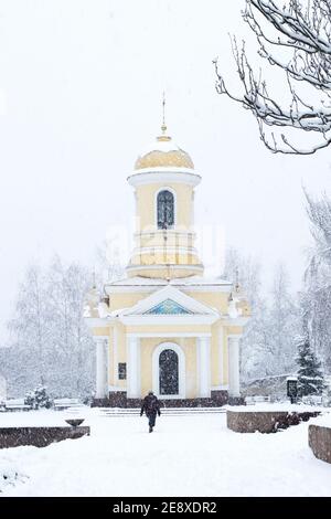 Neige d'hiver dans la ville. Paysage urbain. Chapelle chrétienne sous la neige dans la ville. Une femme marche sous la neige jusqu'à l'église. Blizzard. Banque D'Images