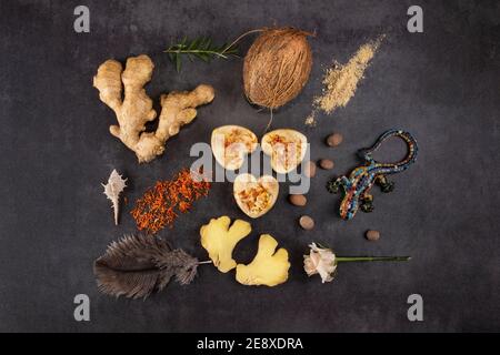 Trois morceaux de savon naturel fait main à côté de morceaux de gingembre, d'épices, de fleurs et d'herbes sur une table en pierre sombre. Divers ingrédients pour les soins de la peau et Banque D'Images