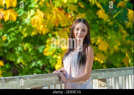Une jeune femme se pose le long de la rampe d'un pont avec des feuilles de chute en arrière-plan. Banque D'Images