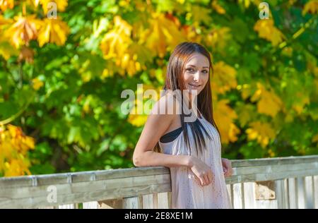 Une jeune femme se pose le long de la rampe d'un pont avec des feuilles de chute en arrière-plan. Banque D'Images