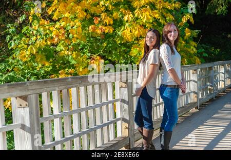 Mère et fille posent sur un pont avec des feuilles d'automne en arrière-plan. Banque D'Images