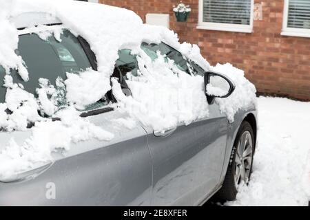 gros plan d'une voiture gris argenté recouverte de neige garée allée devant les fenêtres de la maison pendant les hivers froids jour Banque D'Images