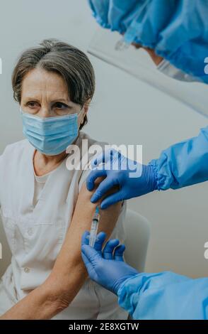 Un médecin de sexe masculin dans un ensemble de protection, un masque et des gants qui font la vaccination COVID-19 pour la femme mature d'un professionnel de la santé à l'hôpital. Banque D'Images