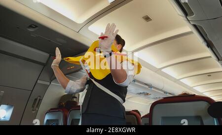 Femme hôtesse de vol sous masque facial présentant la gilet de sauvetage à bord avant le départ du vol. Banque D'Images