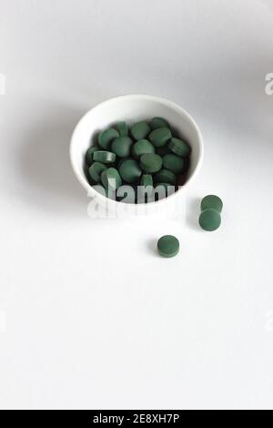 Pilules de spiruline verte dans un bol sur fond blanc, composition minimaliste avec supplément alimentaire végétalien organique végétal et arc-en-ciel de lumière, gros plan, il Banque D'Images