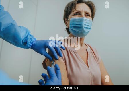 Médecin dans l'ensemble de protection et les gants faisant la vaccination COVID-19 Banque D'Images