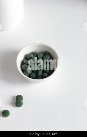 Pilules de spiruline verte dans un bol sur fond blanc, composition minimaliste avec supplément alimentaire végétalien organique végétal et arc-en-ciel de lumière, gros plan, il Banque D'Images