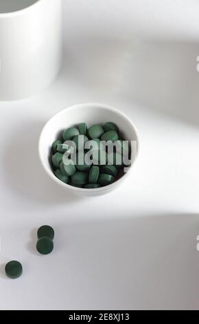 Pilules de spiruline verte dans un bol sur fond blanc, composition minimaliste avec supplément alimentaire végétalien organique végétal et arc-en-ciel de lumière, gros plan, il Banque D'Images