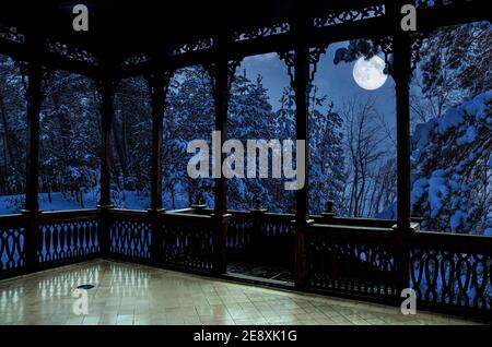 Vue depuis une galerie en bois ajourée ou un belvédère de paysage d'hiver avec des pins et des sapins couverts de neige dans un clair de lune en soirée étoilée. Forêt de conifères Banque D'Images