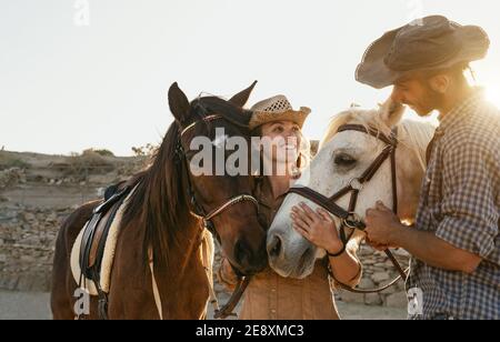 Couple heureux de s'amuser avec les chevaux à l'intérieur de l'écurie - Jeune Agriculteurs partageant du temps avec des animaux dans le ranch corral - humain et animaux concept de style de vie Banque D'Images