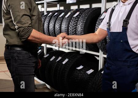 vendeur et client qui se secouent dans un atelier de service automobile, homme fait le choix, achetant des pneus de voiture pour l'hiver Banque D'Images