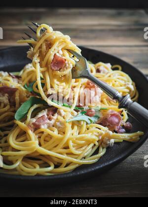 Fourchette avec spaghetti carbonara dans une casserole noire sur une table en bois. Gros plan. Copier l'espace. Tir vertical. Banque D'Images
