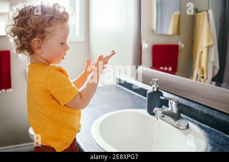 Un petit garçon du Caucase se lavant les mains dans la salle de bains à la maison. Hygiène de santé et routine matinale pour les enfants. Mignon drôle enfant jouant avec l'eau. Banque D'Images