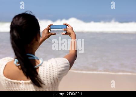 Femme afro-américaine sur une plage prenant la photo du sea avec smartphone Banque D'Images