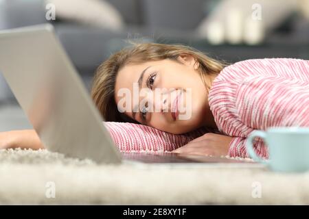 Femme sincère regardant les médias sur un ordinateur portable couché sur le sol dans le salon à la maison Banque D'Images