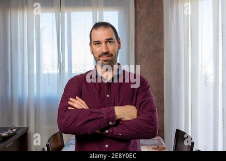 Jeune homme beau barbu portant une chemise bordeaux heureux visage souriant avec des bras croisés regardant la caméra. Concept de positivité Banque D'Images