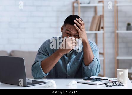 Black Man Blowing Nose dans Napkin assis dans le bureau Banque D'Images