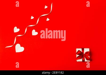 Composition de la Saint-Valentin. Cœur en papier blanc et petite boîte cadeau blanche avec ruban rouge sur fond rouge et style de pose à plat. Concept de la Saint-Valentin Banque D'Images