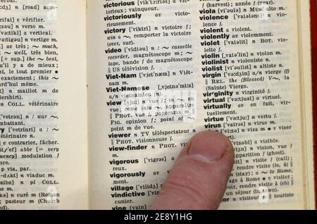 Un seul doigt pointant vers le mot virus sur un anglais Dictionnaire français page imprimée qui est d'origine latine la même chose dans les deux langues Banque D'Images