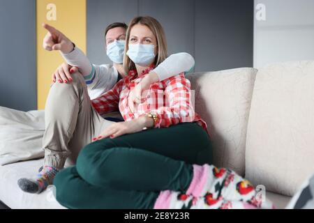 Mari et femme assis sur un canapé avec des masques médicaux de protection Banque D'Images